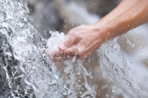 Hands cooling down with fresh and clean water from a waterfall
